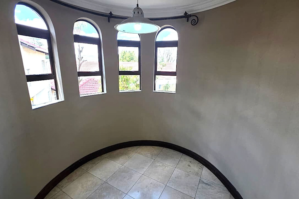A bright, curved living space featuring arched windows, neutral tiled flooring, and a central pendant light fixture.