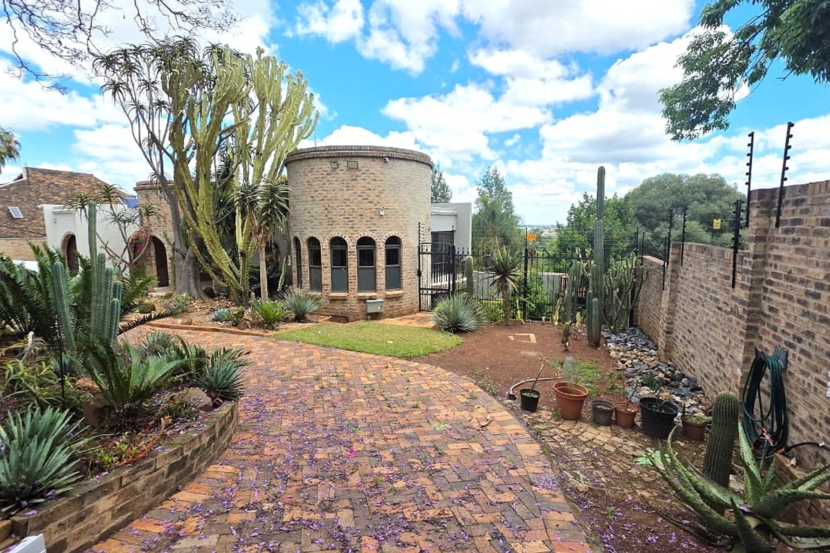 A well-maintained rear garden area featuring a unique cylindrical brick structure, paved pathways, and established succulent landscaping enclosed by a brick boundary wall.