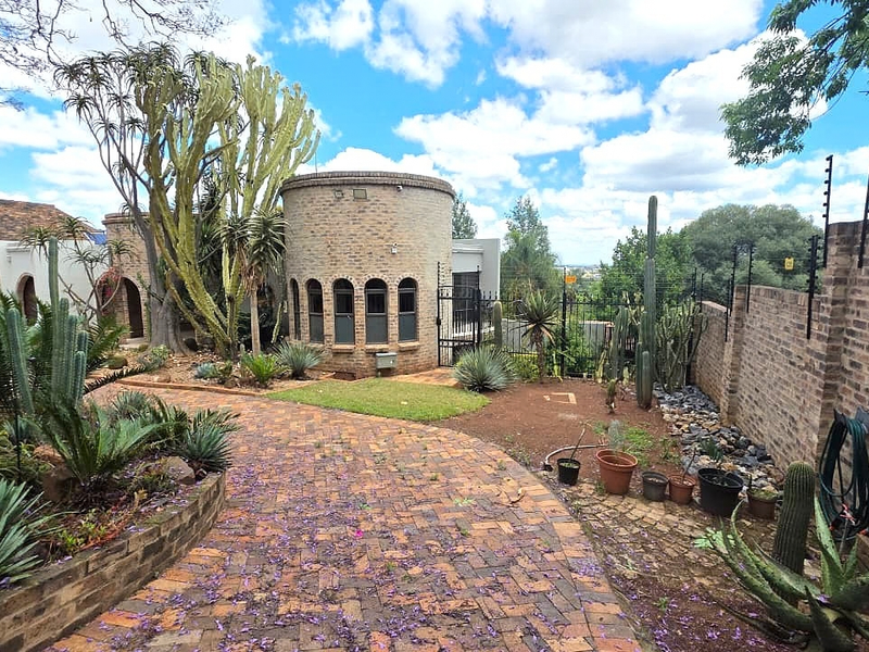 A well-maintained rear garden area featuring a unique cylindrical brick structure, paved pathways, and established succulent landscaping enclosed by a brick boundary wall.