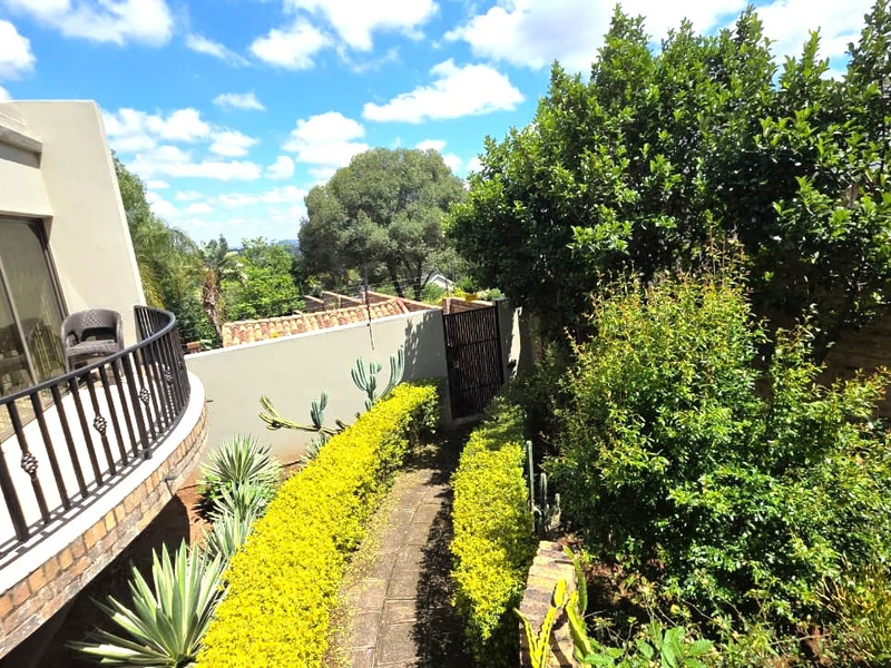 Rear exterior view featuring a curved balcony with wrought iron railings, sliding glass doors, and a landscaped garden path leading to a boundary wall.
