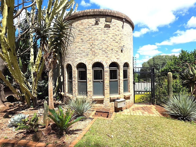 A unique circular brick structure featuring arched windows, set within a landscaped garden with mature succulents and secure perimeter fencing.
