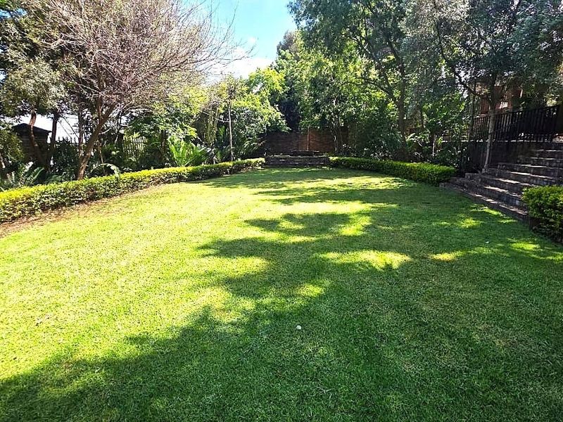 A well-maintained, spacious garden featuring a lush green lawn, mature trees, established hedging, and brick stairs leading to an elevated area.