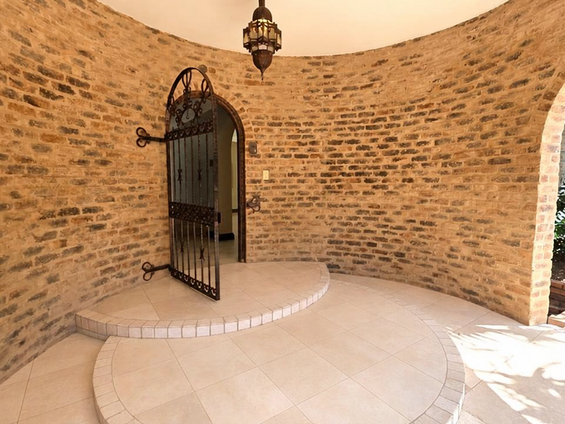 A unique curved brick entrance foyer featuring a decorative wrought iron security gate, raised tiled platform, and a classic pendant light fixture.