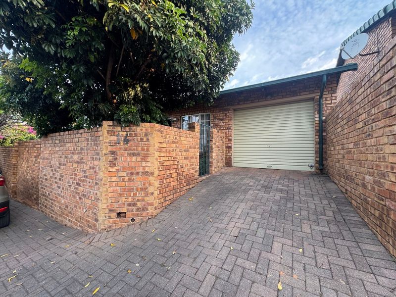 Front exterior view of the townhouse featuring a paved driveway, brick boundary wall, and a secure roller garage door.