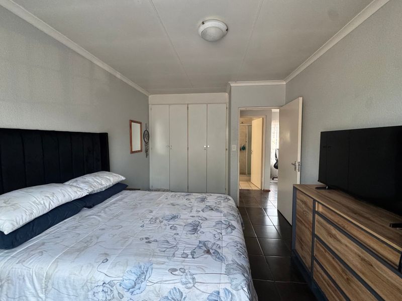 A functional bedroom featuring built-in cupboards, tiled flooring, and direct access to an adjoining bathroom.