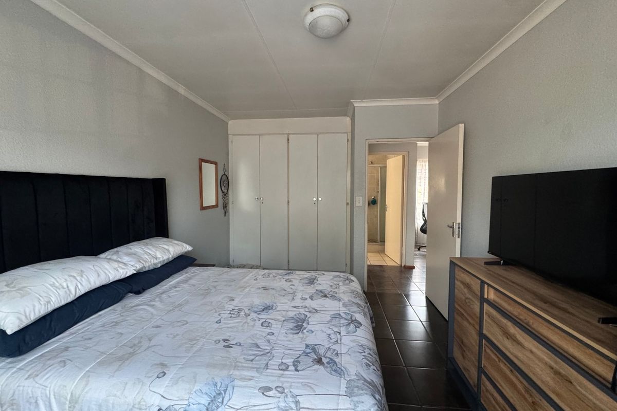 A functional bedroom featuring built-in cupboards, tiled flooring, and direct access to an adjoining bathroom.