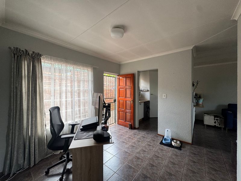 A functional living area featuring tiled flooring, a timber exterior door with security gate, and access to an adjacent utility or laundry space.