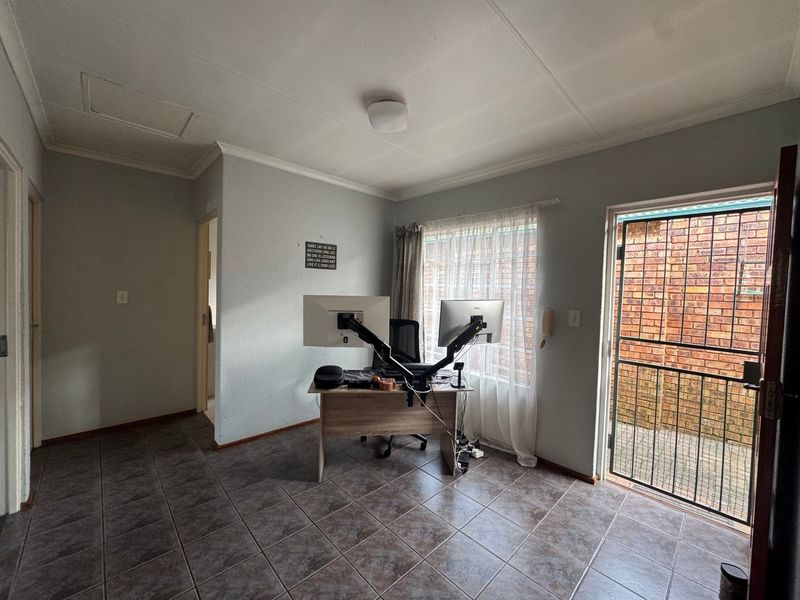 A functional office space featuring tiled flooring, a security gate, and direct access to the exterior.