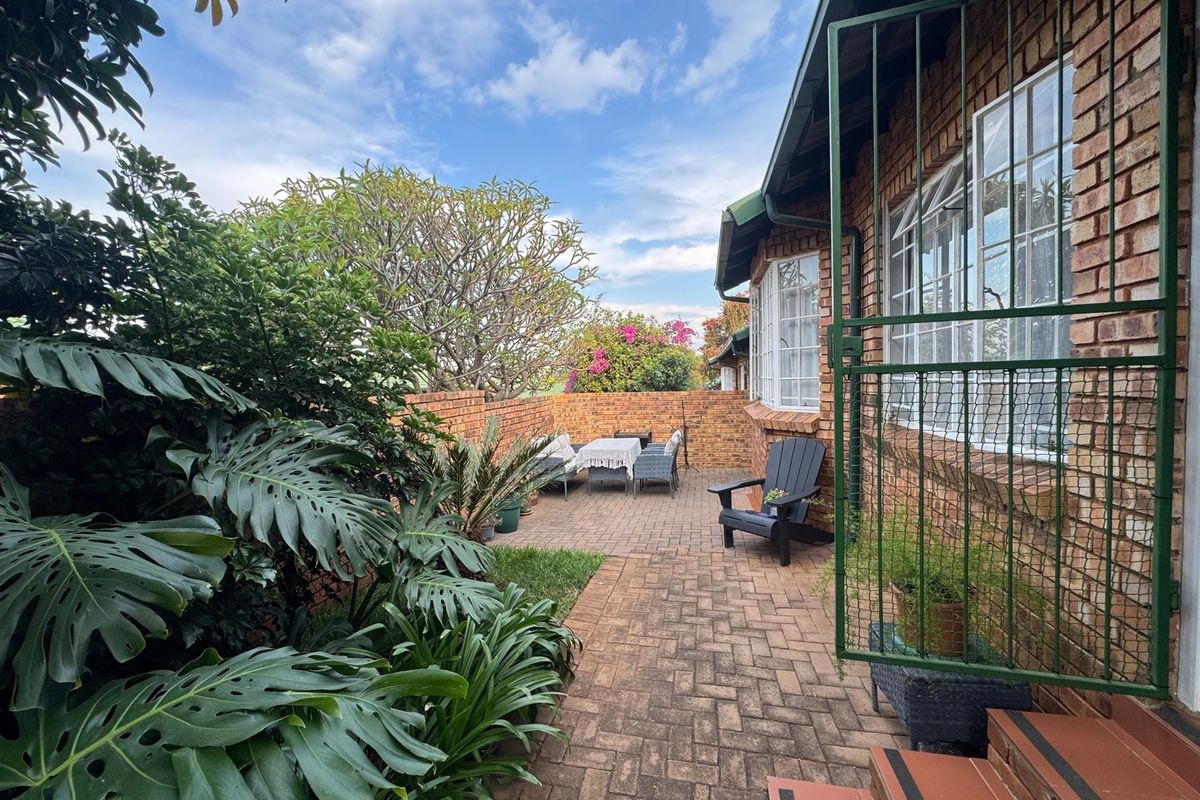 A private rear courtyard featuring brick paving, established garden greenery, and a secure gated entrance leading to the townhouse exterior.