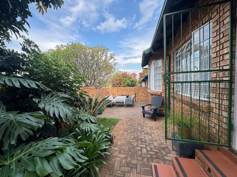 A private rear courtyard featuring brick paving, established garden greenery, and a secure gated entrance leading to the townhouse exterior.