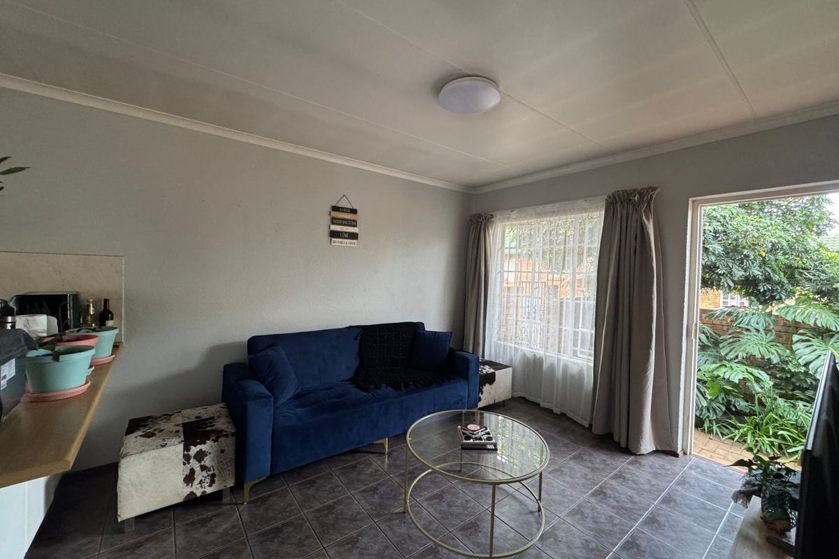 A living room featuring tiled flooring, a ceiling light, and a sliding glass door providing access to the garden area.