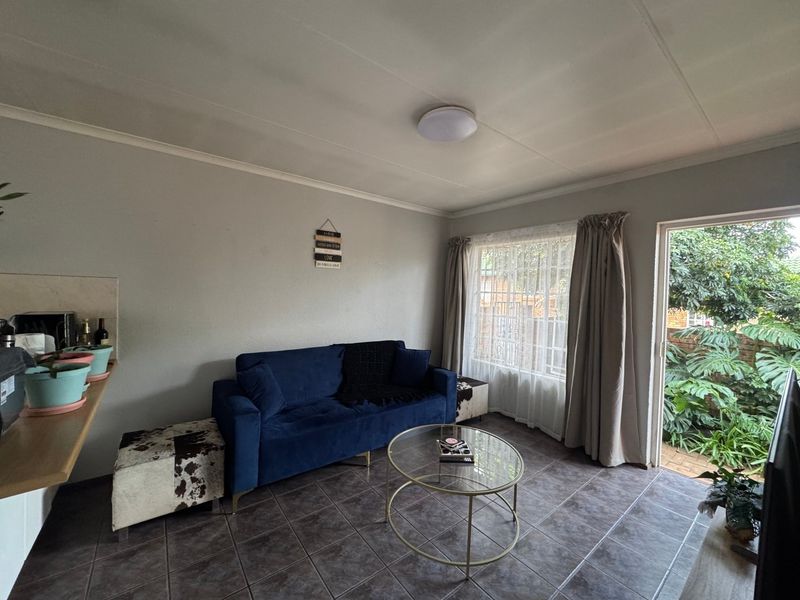 A living room featuring tiled flooring, a ceiling light, and a sliding glass door providing access to the garden area.