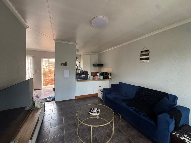 Open-plan living area featuring tiled flooring, a compact kitchen corner with built-in cabinetry, and direct access to an outdoor patio area.