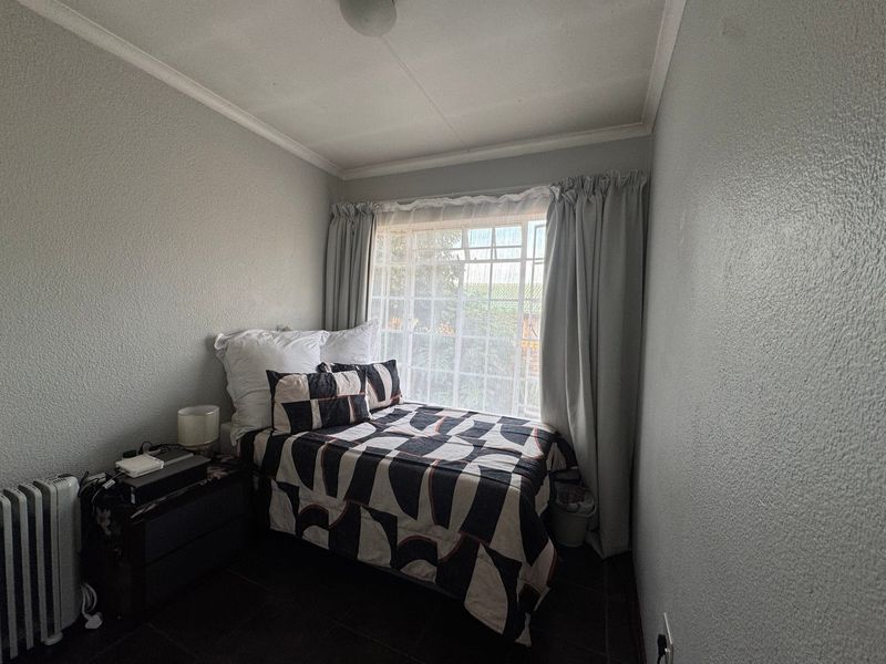 A compact bedroom featuring tiled flooring, a window with security bars, and neutral wall finishes, offering a functional space for a single bed.