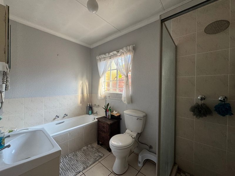 A functional bathroom featuring a built-in bathtub, a separate shower enclosure with a rain shower head, and tiled finishes.