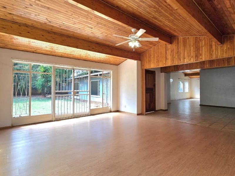Spacious living area featuring exposed timber ceiling beams, a stone fireplace, and large sliding glass doors that provide ample natural light and garden access.