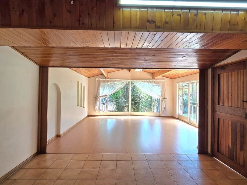Spacious, empty living area featuring a distinctive timber-clad ceiling, tiled and laminate flooring, and large windows providing ample natural light.