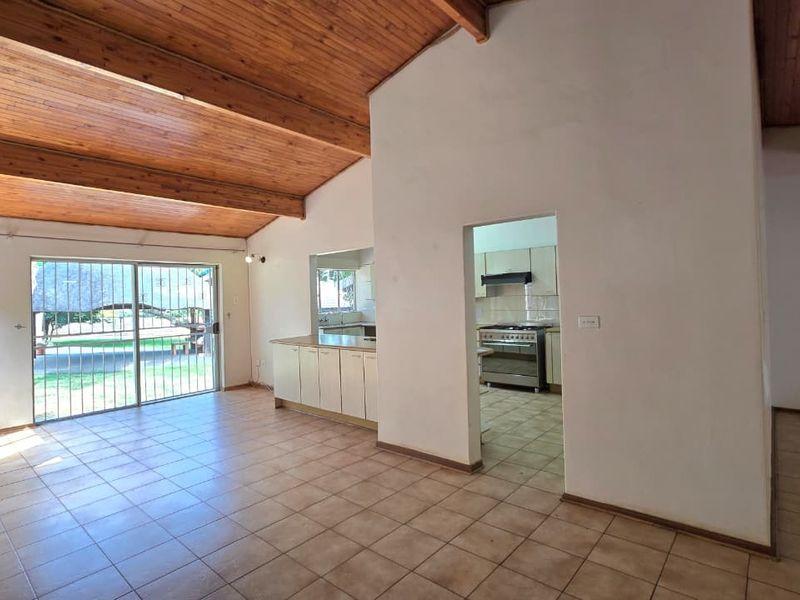 Spacious open-plan living area featuring high exposed timber beam ceilings, tiled flooring, and a functional kitchen with built-in cabinetry and a gas stove.