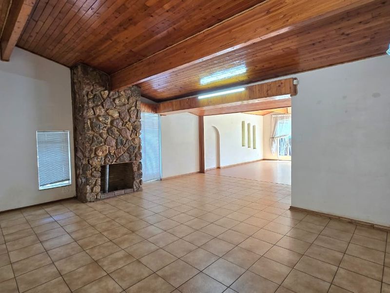 Spacious open-plan living area featuring a prominent stone fireplace, exposed timber ceilings, and neutral tiled flooring, offering a versatile layout for modern living.