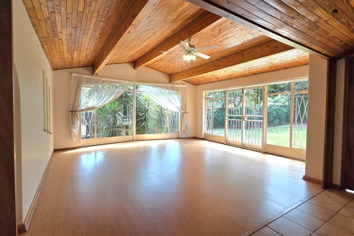 Spacious living area featuring a vaulted timber ceiling, ceiling fan, and large glass sliding doors that provide ample natural light and garden access.