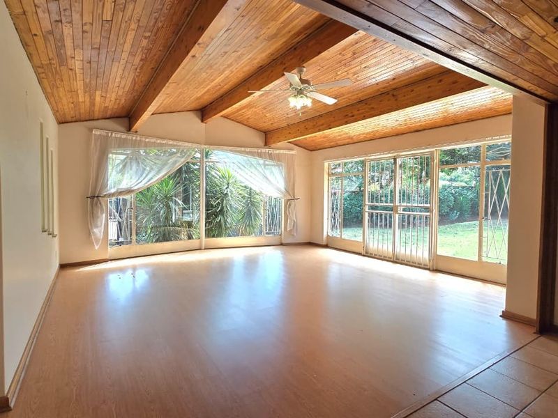 Spacious living area featuring a vaulted timber ceiling, ceiling fan, and large glass sliding doors that provide ample natural light and garden access.