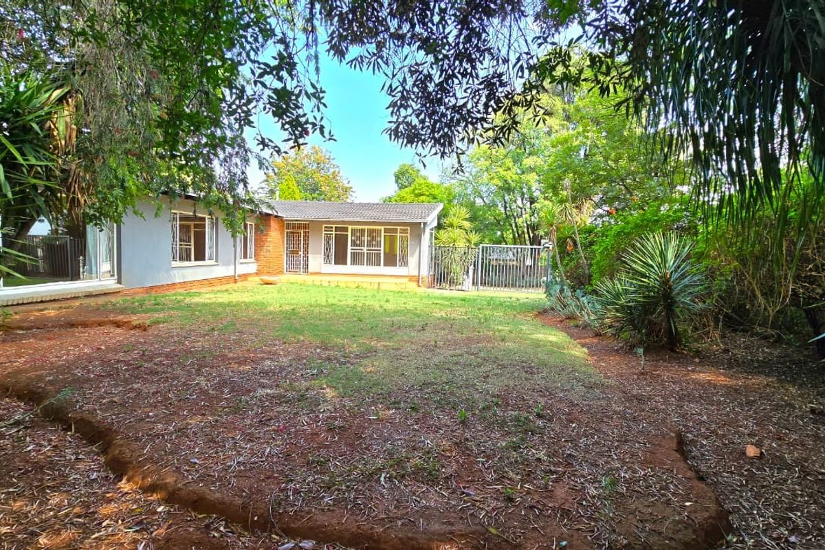 A view of the rear garden and house exterior, featuring a lawn area, mature trees, and secure metal gate access.