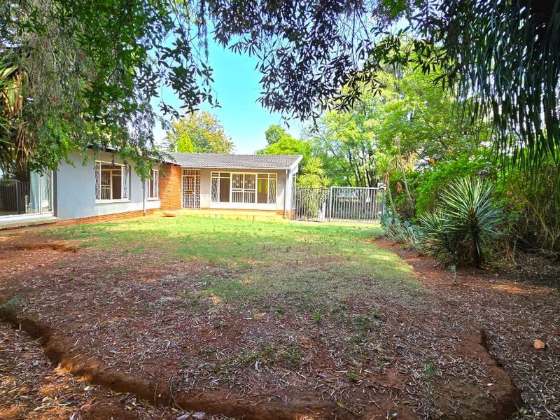 A view of the rear garden and house exterior, featuring a lawn area, mature trees, and secure metal gate access.