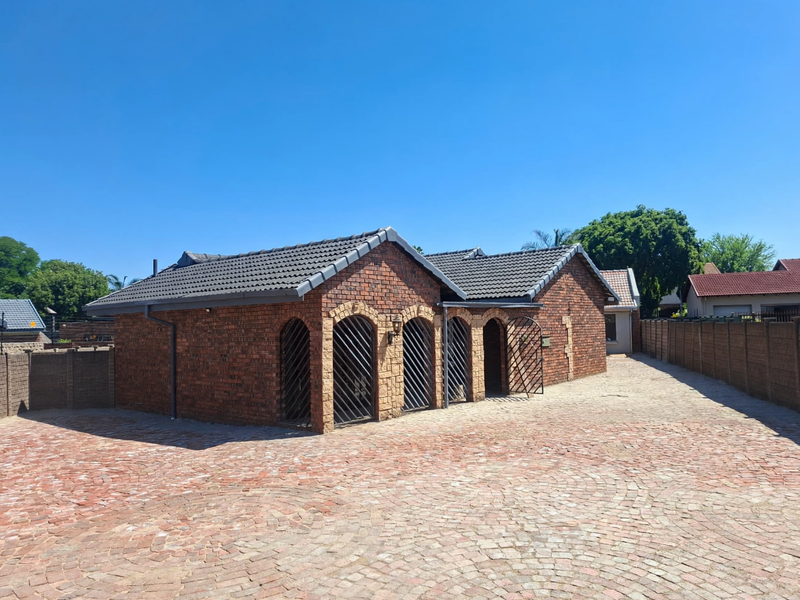 A well-maintained face brick building featuring arched entrances with security gates, set within a spacious paved courtyard area.