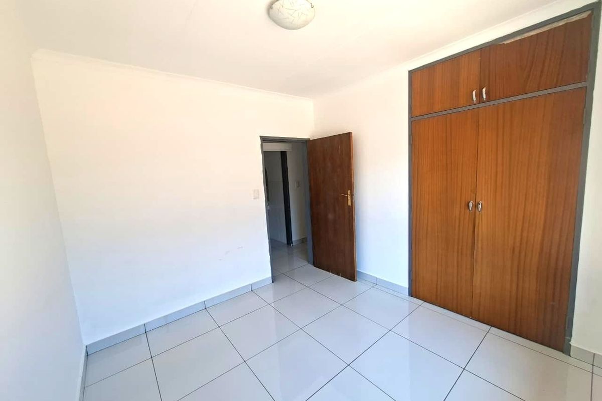 A clean, empty bedroom featuring neutral tiled flooring and built-in wooden cupboards, offering a blank canvas for personalization.