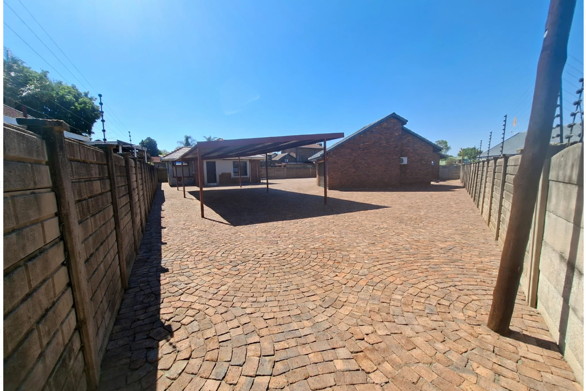 Spacious rear yard featuring extensive brick paving, a functional carport structure, and secure perimeter boundary walls with electric fencing.