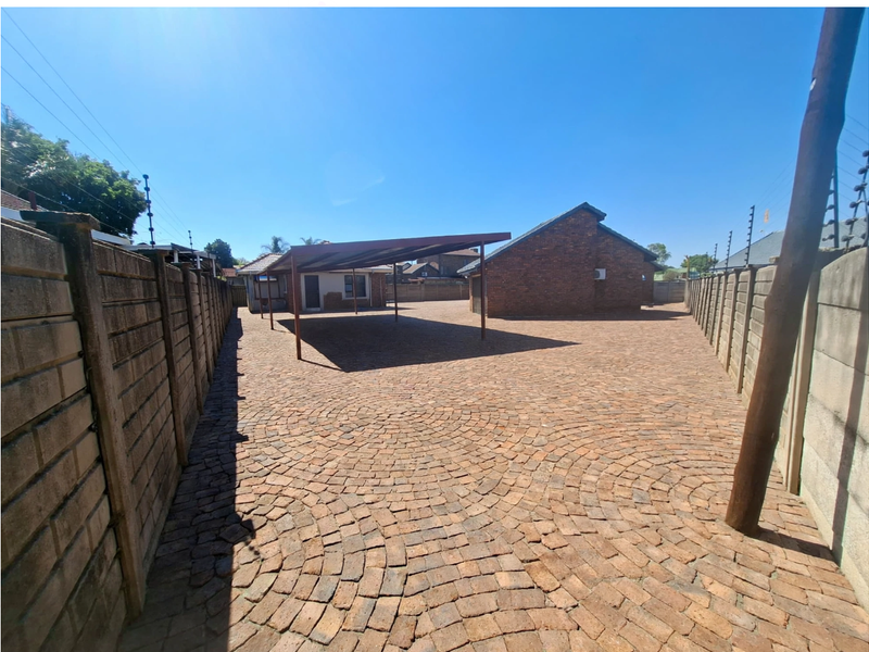 Spacious rear yard featuring extensive brick paving, a functional carport structure, and secure perimeter boundary walls with electric fencing.