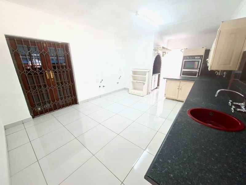 An empty kitchen featuring tiled flooring, built-in cabinetry, a double sink, and a built-in oven, with direct access through a security gate.