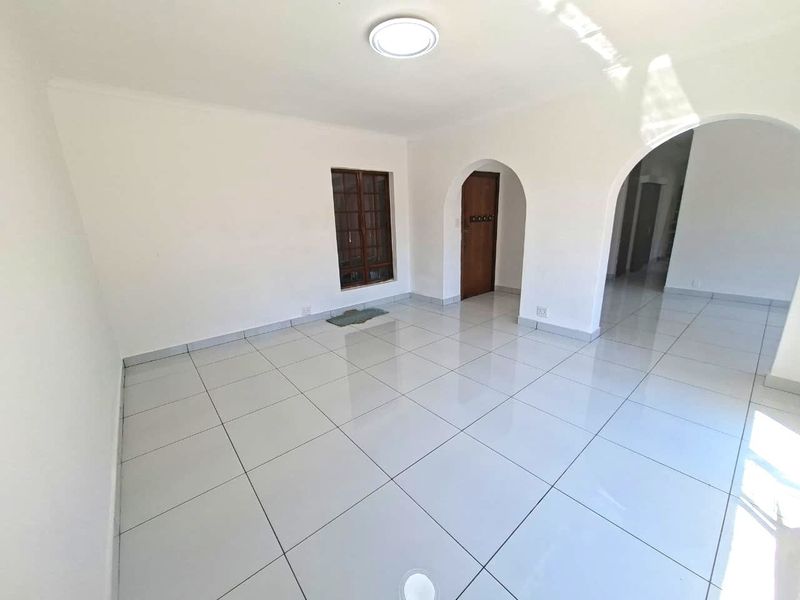 A bright, empty living area featuring white tiled flooring, arched architectural doorways, and a clean, neutral aesthetic ready for personalization.