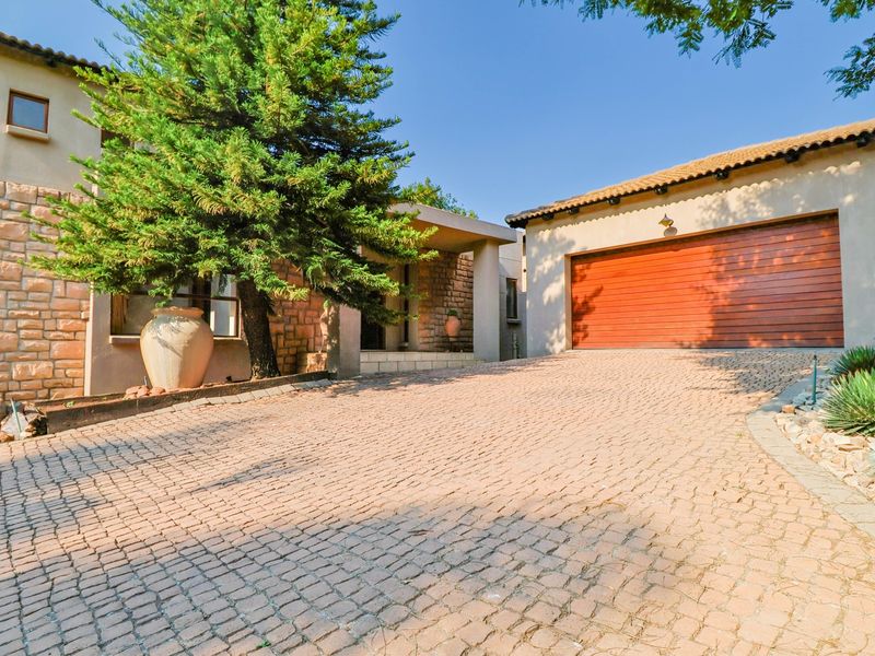 Front elevation featuring a cobblestone driveway, double garage, and stone-clad facade with a covered entrance.
