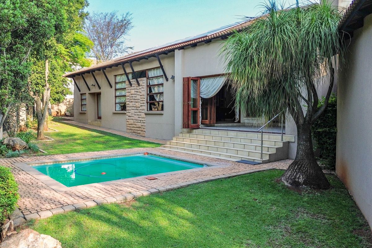 Rear exterior view featuring a swimming pool, brick paved surround, stone-clad facade, and tiled steps leading to the main living area.