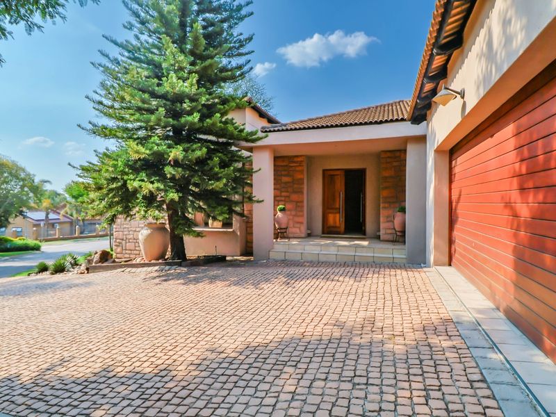 Front elevation of a house featuring a cobblestone driveway, double garage, stone-clad entrance, and a covered porch area.