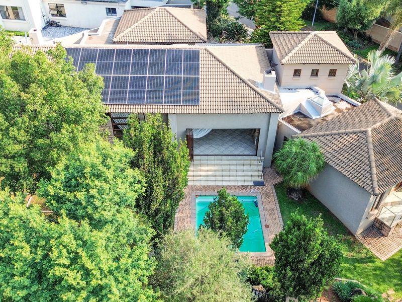 Aerial view of the property featuring a tiled roof with solar panels, a swimming pool, a paved patio area, and established garden surroundings.