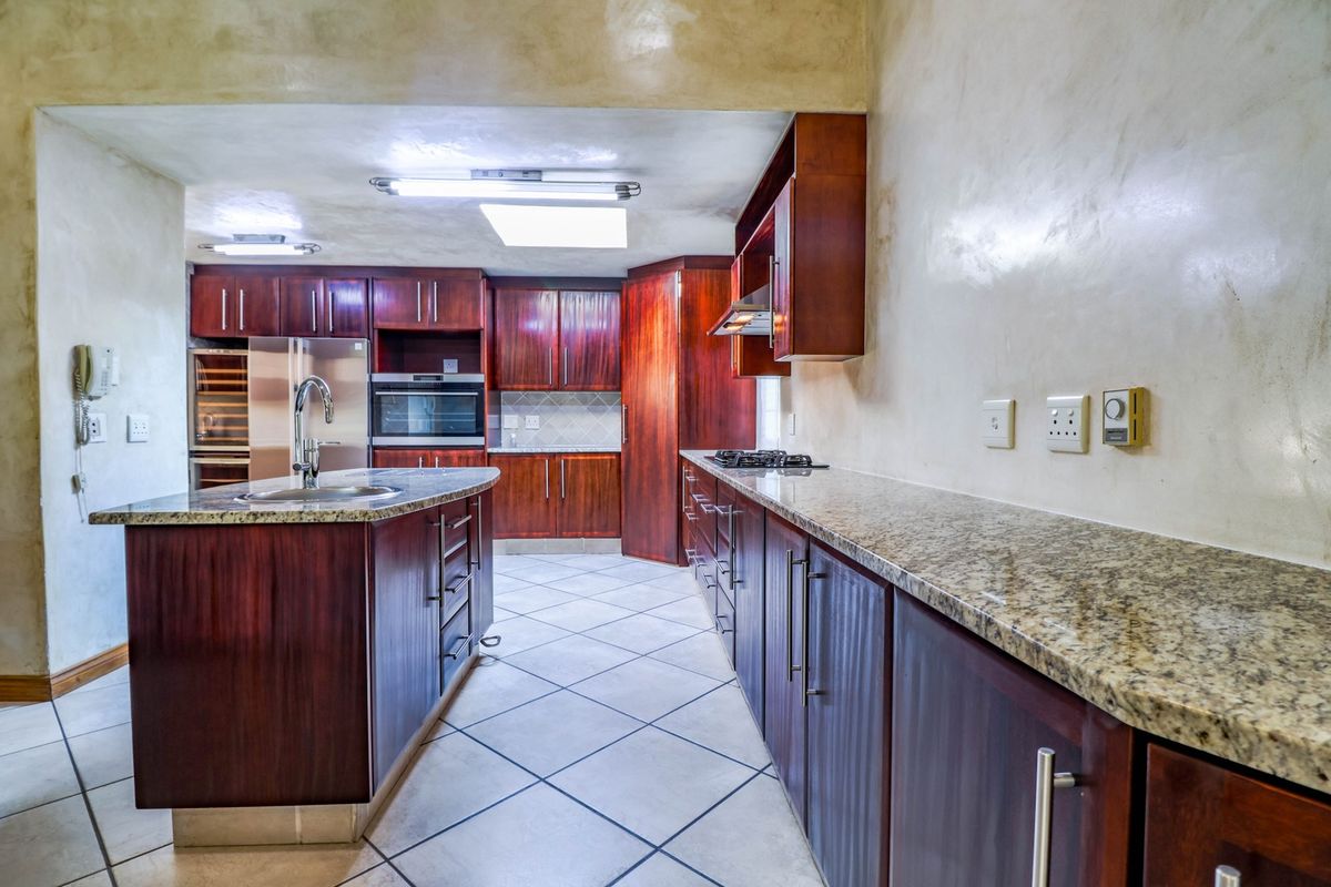 Spacious kitchen featuring dark wood cabinetry, granite countertops, a central island with a sink, built-in oven, gas hob, and a skylight for natural light.