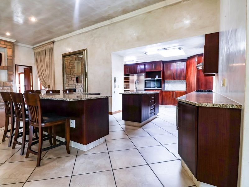 Spacious open-plan kitchen and dining area featuring dark wood cabinetry, granite countertops, a central island, and an adjacent stone fireplace.