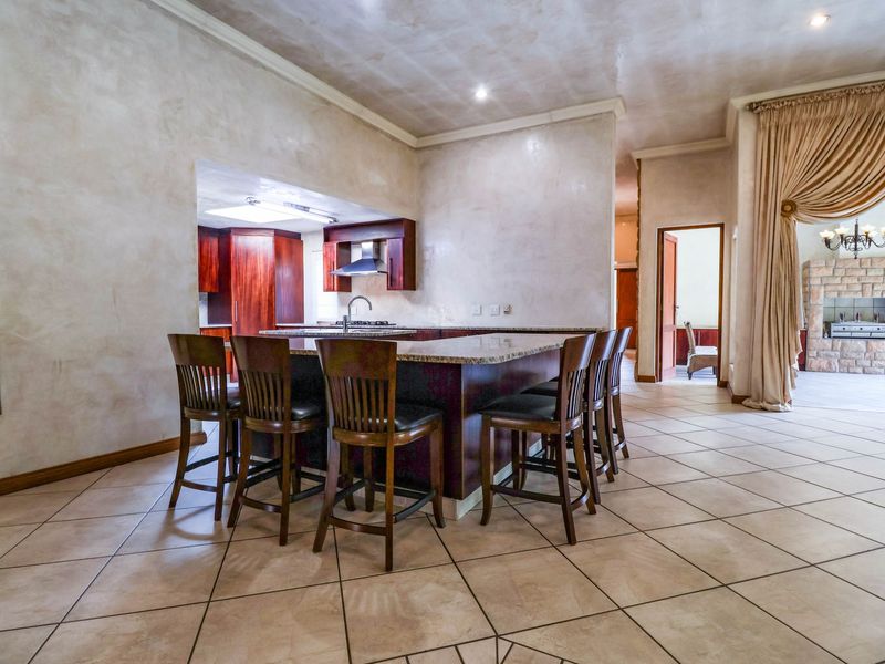 Spacious open-plan kitchen and living area featuring a large granite island, custom cabinetry, tiled floors, and a prominent stone fireplace in the adjacent room.