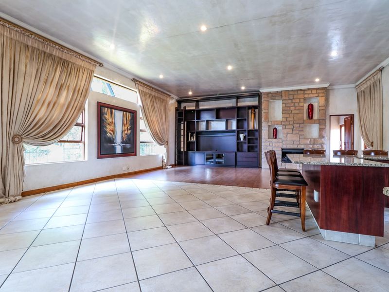 Spacious open-plan living area featuring a stone fireplace, built-in shelving, and a granite kitchen island with tiled and laminate flooring.