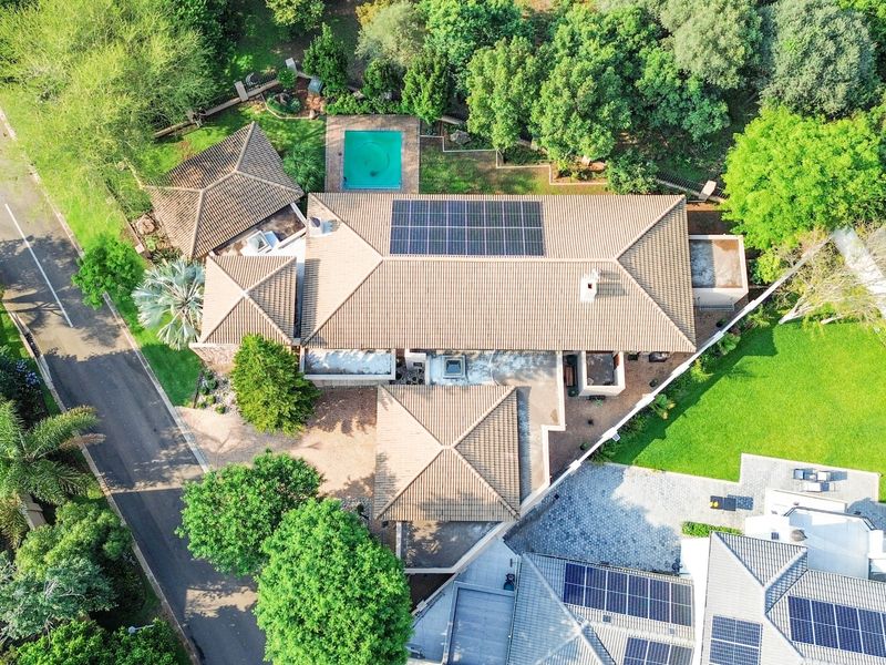 Aerial view of the property showcasing the tiled roof with solar panels, swimming pool, landscaped garden, and paved driveway access.