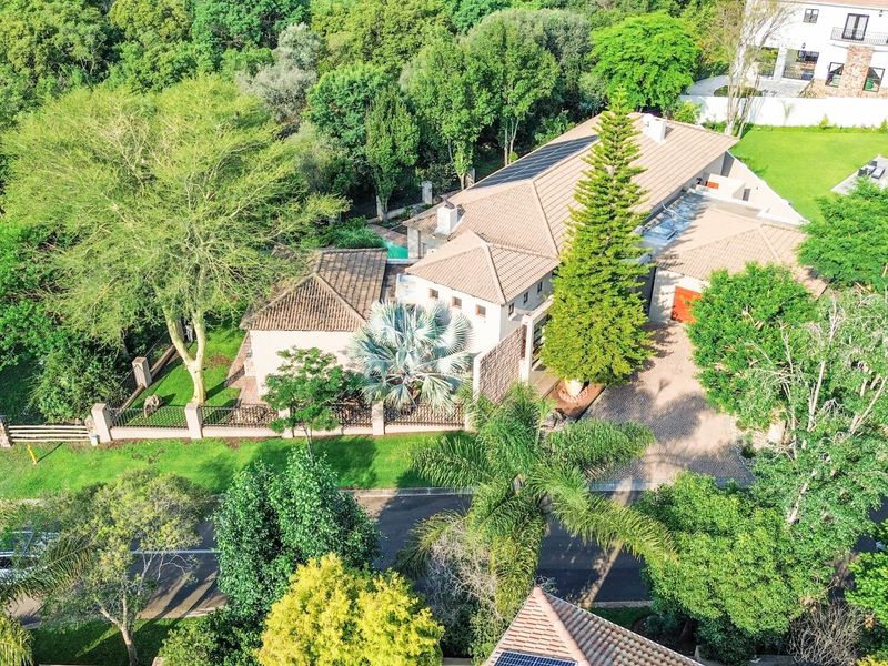 An aerial view of a residential property featuring a tiled roof with solar panels, a paved driveway, and established garden landscaping.