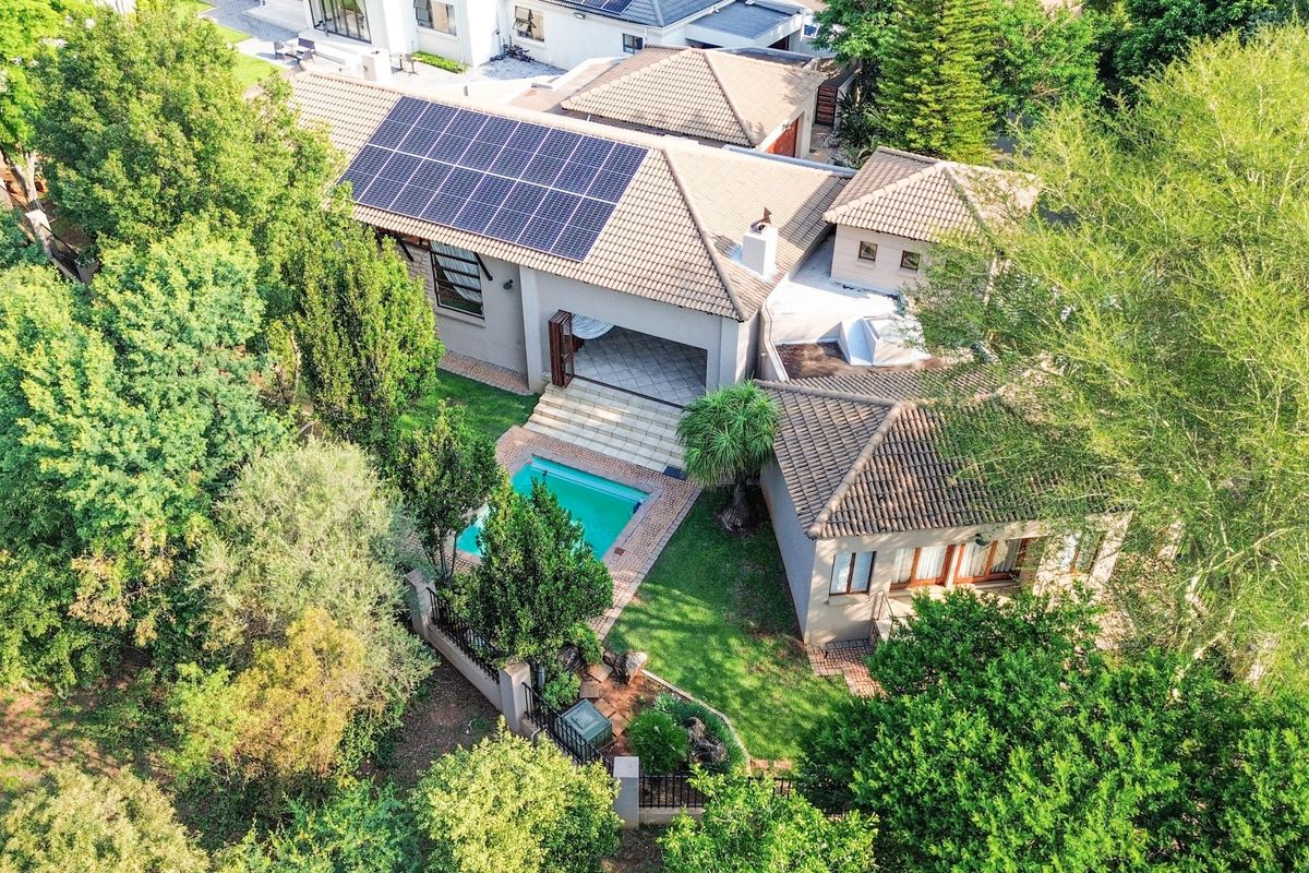 Aerial view of the property featuring a tiled roof with solar panels, a swimming pool, and a landscaped garden with a covered patio area.