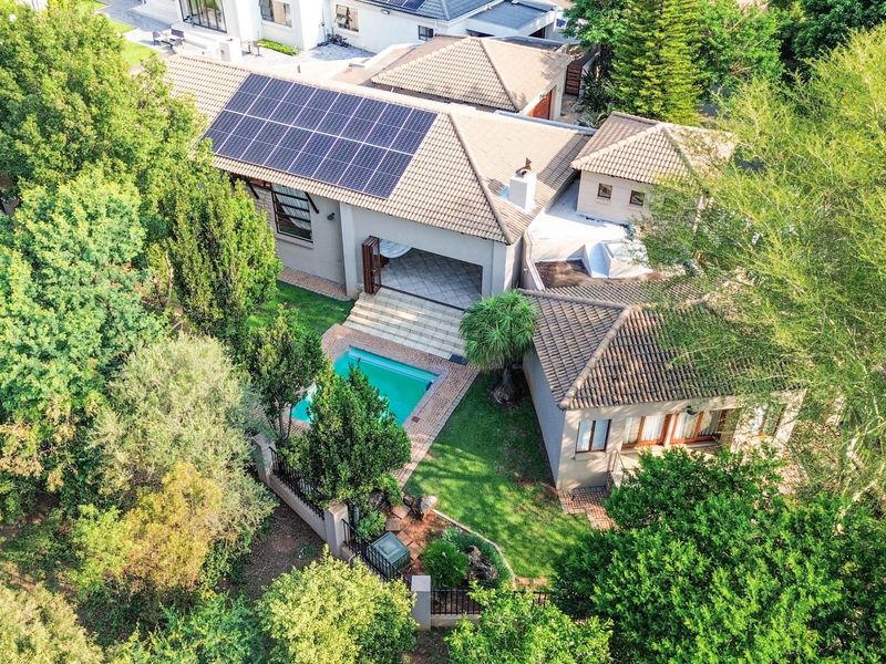 Aerial view of the property featuring a tiled roof with solar panels, a swimming pool, and a landscaped garden with a covered patio area.