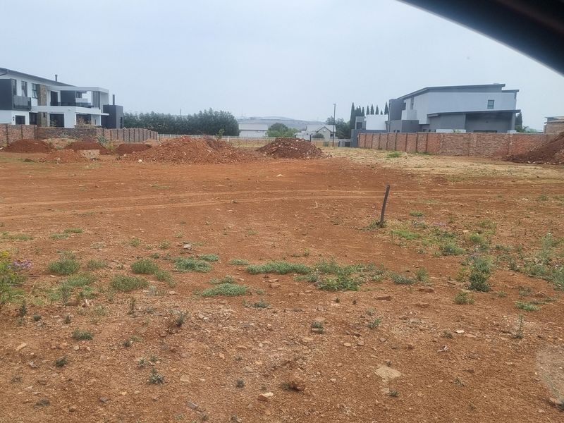 A vacant residential plot of land featuring red soil, surrounded by brick boundary walls in a developing estate.