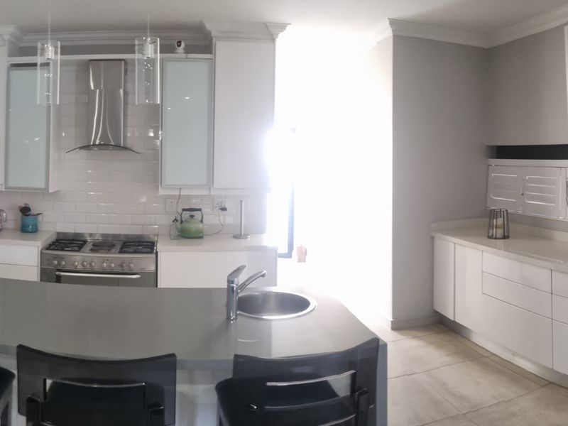 Modern kitchen featuring white cabinetry, stone countertops, a central island with sink, stainless steel appliances, and a subway tile backsplash.