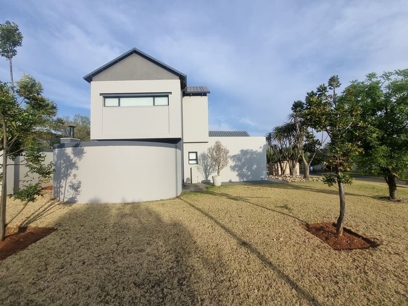 A view of the rear elevation of a modern house featuring a distinctive curved wall, metal roofing, and a well-maintained garden area.