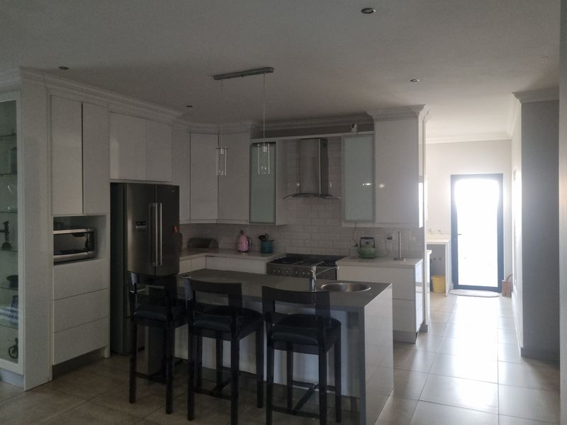 Modern kitchen featuring white cabinetry, a central island with a sink, stainless steel appliances, and a subway tile backsplash, leading to a rear exit.