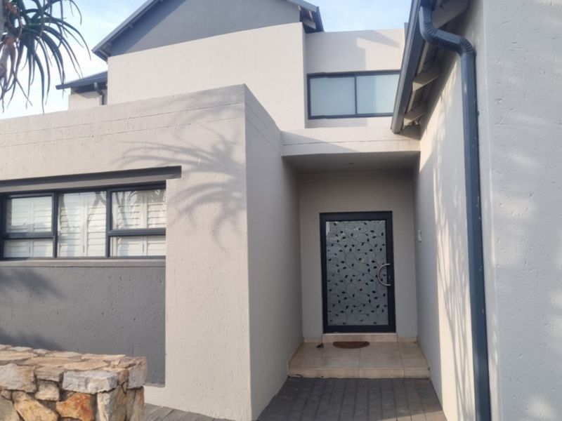 Modern front entrance featuring a decorative glass door, stone cladding accents, and clean architectural lines with neutral exterior paint.